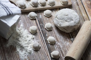 Hamur köftesi pişiriyorum. Çiğ hamur köfteleri tahta bir tahtanın üzerinde yatıyor. Yakınlarda un, merdane ve hamuru bir ahşap zemin üzerinde yatıyor..