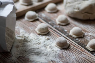 Hamur köftesi pişiriyorum. Çiğ hamur köfteleri tahta bir tahtanın üzerinde yatıyor. Yakınlarda un, merdane ve hamuru bir ahşap zemin üzerinde yatıyor..