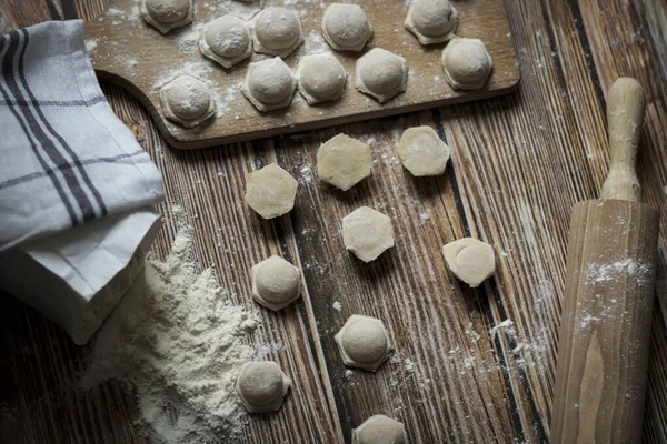 Hamur köftesi pişiriyorum. Çiğ hamur köfteleri tahta bir tahtanın üzerinde yatıyor. Yakınlarda un, merdane ve hamuru bir ahşap zemin üzerinde yatıyor..