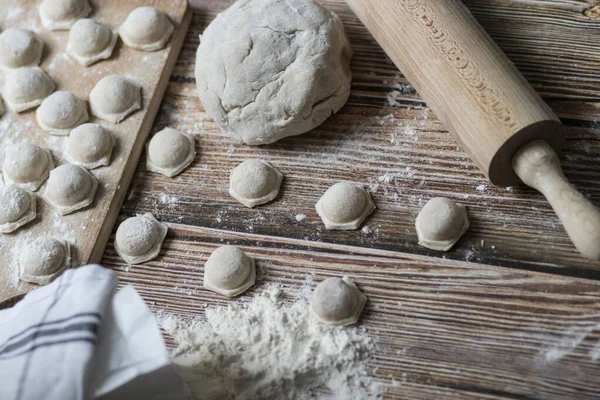Hamur köftesi pişiriyorum. Çiğ hamur köfteleri tahta bir tahtanın üzerinde yatıyor. Yakınlarda un, merdane ve hamuru bir ahşap zemin üzerinde yatıyor..