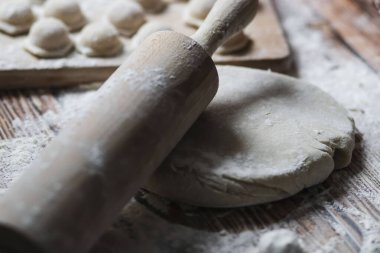 Hamur köftesi pişiriyorum. Çiğ hamur köfteleri tahta bir tahtanın üzerinde yatıyor. Yakınlarda un, merdane ve hamuru bir ahşap zemin üzerinde yatıyor..