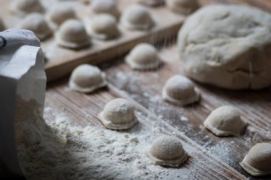 Hamur köftesi pişiriyorum. Çiğ hamur köfteleri tahta bir tahtanın üzerinde yatıyor. Yakınlarda un, merdane ve hamuru bir ahşap zemin üzerinde yatıyor..