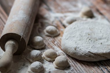 Hamur köftesi pişiriyorum. Çiğ hamur köfteleri tahta bir tahtanın üzerinde yatıyor. Yakınlarda un, merdane ve hamuru bir ahşap zemin üzerinde yatıyor..