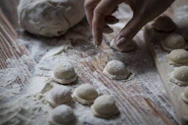 Hamur köftesi pişiriyorum. Çiğ hamur köfteleri tahta bir tahtanın üzerinde yatıyor. Yakınlarda un, merdane ve hamuru bir ahşap zemin üzerinde yatıyor..