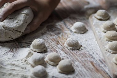 Hamur köftesi pişiriyorum. Çiğ hamur köfteleri tahta bir tahtanın üzerinde yatıyor. Yakınlarda un, merdane ve hamuru bir ahşap zemin üzerinde yatıyor..