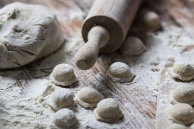 Hamur köftesi pişiriyorum. Çiğ hamur köfteleri tahta bir tahtanın üzerinde yatıyor. Yakınlarda un, merdane ve hamuru bir ahşap zemin üzerinde yatıyor..