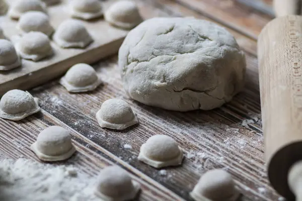 Hamur köftesi pişiriyorum. Çiğ hamur köfteleri tahta bir tahtanın üzerinde yatıyor. Yakınlarda un, merdane ve hamuru bir ahşap zemin üzerinde yatıyor..