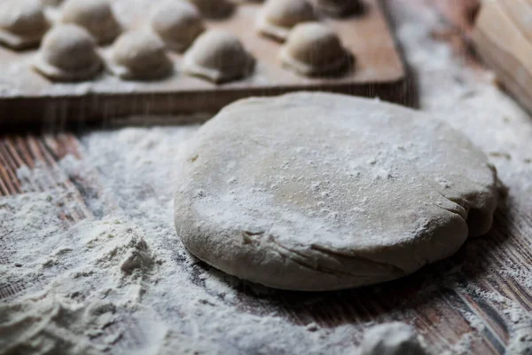 Hamur köftesi pişiriyorum. Çiğ hamur köfteleri tahta bir tahtanın üzerinde yatıyor. Yakınlarda un, merdane ve hamuru bir ahşap zemin üzerinde yatıyor..