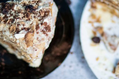 Napolion keki. Kuru üzümle süslenmiş siyah tabakta bir parça kek. Gri arkaplanı olan bir masanın üzerinde durur