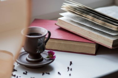 Pencerenin yanında güzel bir kahve fincanı var. Yakınlarda da kitaplar var.