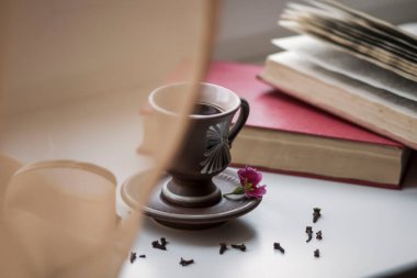 Pencerenin yanında güzel bir kahve fincanı var. Yakınlarda da kitaplar var.