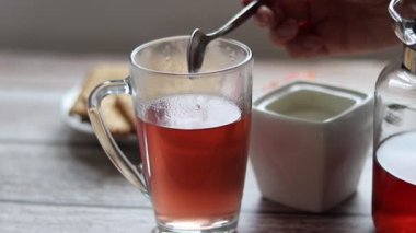 Şeffaf bir fincana meyve çayı döküyorum. Arka planda kurabiye ve şeker kasesi var..