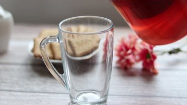 Şeffaf bir fincana meyve çayı döküyorum. Arka planda kurabiye ve şeker kasesi var..