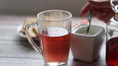 Şeffaf bir fincana meyve çayı döküyorum. Arka planda kurabiye ve şeker kasesi var..