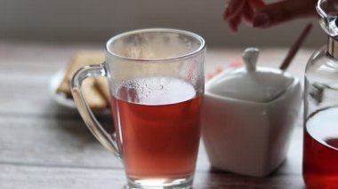 Şeffaf bir fincana meyve çayı döküyorum. Arka planda kurabiye ve şeker kasesi var..