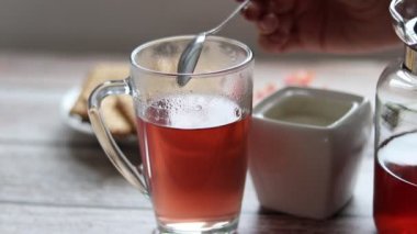 Şeffaf bir fincana meyve çayı döküyorum. Arka planda kurabiye ve şeker kasesi var..