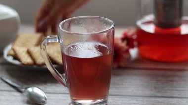 Şeffaf bir fincana meyve çayı döküyorum. Arka planda kurabiye ve şeker kasesi var..