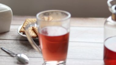 Şeffaf bir fincana meyve çayı döküyorum. Arka planda kurabiye ve şeker kasesi var..