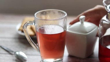 Şeffaf bir fincana meyve çayı döküyorum. Arka planda kurabiye ve şeker kasesi var..