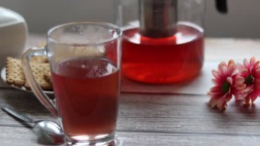 Şeffaf bir fincana meyve çayı döküyorum. Arka planda kurabiye ve şeker kasesi var..