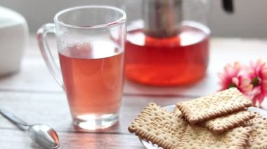 Şeffaf bir fincana meyve çayı döküyorum. Arka planda kurabiye ve şeker kasesi var..