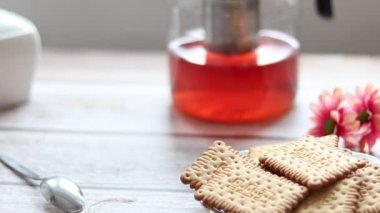 Şeffaf bir fincana meyve çayı döküyorum. Arka planda kurabiye ve şeker kasesi var..