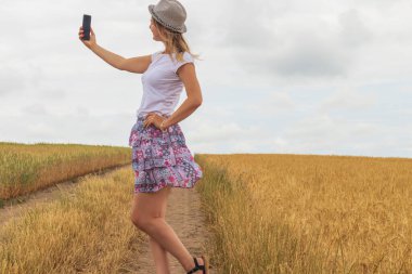 Genç kız buğday tarlasının arka planında selfie çekiyor.