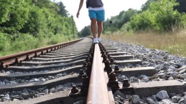 Genç bir adam raylarda yürüyor.