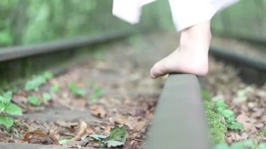 Genç bir kız demiryolunda yalınayak yürüyor. Yaz havası. Ormanın etrafında..