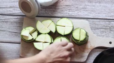 Erkek eller, tahta kesme tahtasının üzerinde bir bıçakla kabak kesiyor. Mutfak masasında.