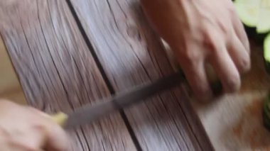 Erkek eller, tahta kesme tahtasının üzerinde bir bıçakla kabak kesiyor. Mutfak masasında.