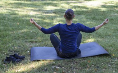 Genç adam parkta yoga pratiği yapıyor. Ağaçların etrafında yeşil ağaçlar var..