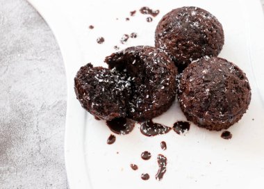 Beyaz tabakta çikolatalı kek. Üstüne çikolata ve hindistan cevizi serpiştirilmiş. Ev yapımı yumuşacık ve sulu çikolatalı kekler. Gri bir arkaplanda