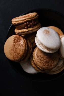 Koyu arkaplanda makaronlar, renkli Fransız kurabiyeleri. Kurabiyeler. Vanilyalı ve çikolatalı tatlı. Sağlıklı vejetaryen şeker yok. 8 Mart - Uluslararası Kadınlar Günü