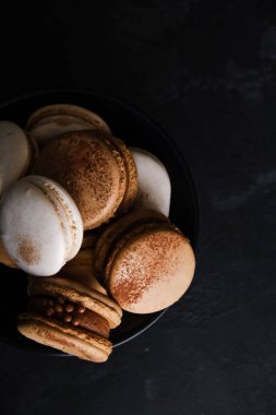 Koyu arkaplanda makaronlar, renkli Fransız kurabiyeleri. Kurabiyeler. Vanilyalı ve çikolatalı tatlı. Sağlıklı vejetaryen şeker yok. 8 Mart - Uluslararası Kadınlar Günü