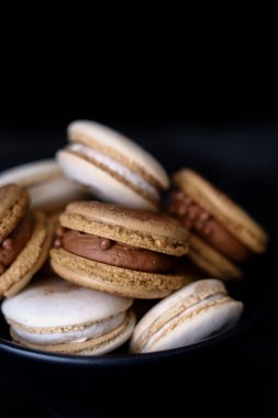 Koyu arkaplanda makaronlar, renkli Fransız kurabiyeleri. Kurabiyeler. Vanilyalı ve çikolatalı tatlı. Sağlıklı vejetaryen şeker yok. 8 Mart - Uluslararası Kadınlar Günü