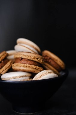 Koyu arkaplanda makaronlar, renkli Fransız kurabiyeleri. Kurabiyeler. Vanilyalı ve çikolatalı tatlı. Sağlıklı vejetaryen şeker yok. 8 Mart - Uluslararası Kadınlar Günü