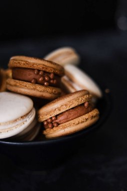Koyu arkaplanda makaronlar, renkli Fransız kurabiyeleri. Kurabiyeler. Vanilyalı ve çikolatalı tatlı. Sağlıklı vejetaryen şeker yok. 8 Mart - Uluslararası Kadınlar Günü