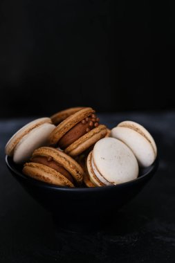 Koyu arkaplanda makaronlar, renkli Fransız kurabiyeleri. Kurabiyeler. Vanilyalı ve çikolatalı tatlı. Sağlıklı vejetaryen şeker yok. 8 Mart - Uluslararası Kadınlar Günü