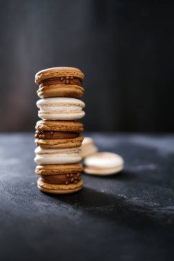 Koyu arkaplanda makaronlar, renkli Fransız kurabiyeleri. Kurabiyeler. Vanilyalı ve çikolatalı tatlı. Sağlıklı vejetaryen şeker yok. 8 Mart - Uluslararası Kadınlar Günü