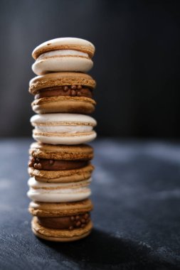 Koyu arkaplanda makaronlar, renkli Fransız kurabiyeleri. Kurabiyeler. Vanilyalı ve çikolatalı tatlı. Sağlıklı vejetaryen şeker yok. 8 Mart - Uluslararası Kadınlar Günü