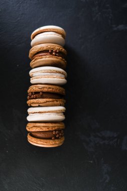 Koyu arkaplanda makaronlar, renkli Fransız kurabiyeleri. Kurabiyeler. Vanilyalı ve çikolatalı tatlı. Sağlıklı vejetaryen şeker yok. 8 Mart - Uluslararası Kadınlar Günü