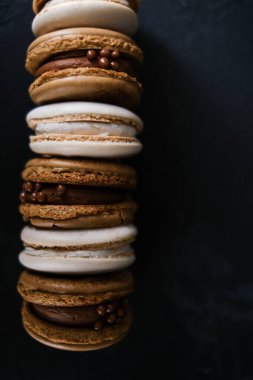 Koyu arkaplanda makaronlar, renkli Fransız kurabiyeleri. Kurabiyeler. Vanilyalı ve çikolatalı tatlı. Sağlıklı vejetaryen şeker yok. 8 Mart - Uluslararası Kadınlar Günü