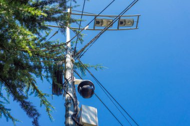 Mavi gökyüzüne karşı bir sokak lambası direğindeki bir demet elektrik kablosu.