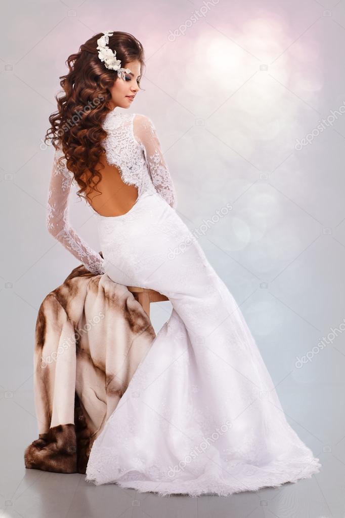 Brunette girl in a wedding dress sits on a mink coat back