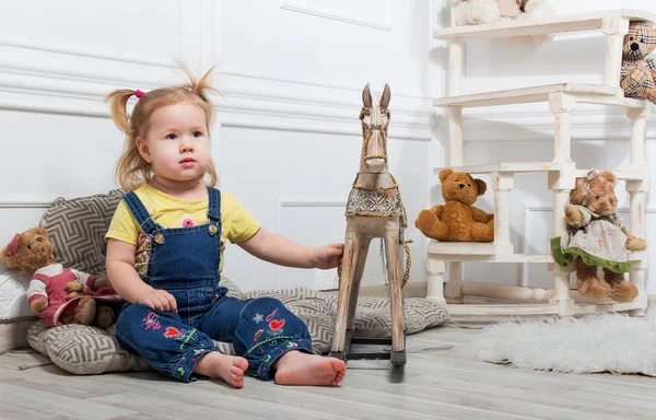 Little girl  surrounded by toys and holds a wooden horse — Stock Photo, Image