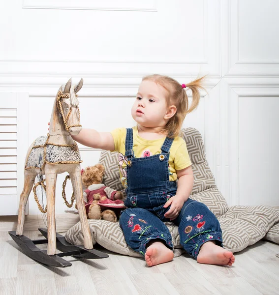 Menina cercada por brinquedos e segura um cavalo de madeira — Fotografia de Stock