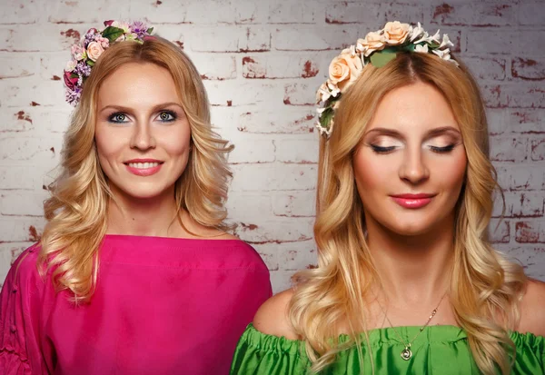 Duas mulheres com grinaldas de Flowers.two menina bonita com maquiagem expressiva e grinaldas de flores em sua cabeça em um fundo de tijolo bege . — Fotografia de Stock