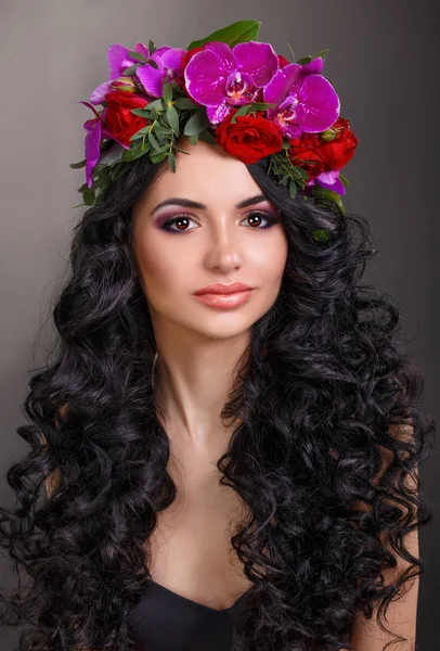 Beautiful girl with a wreath of orchids on head. Glamorous woman in black leather corset. long black curly hair — Stock Photo, Image