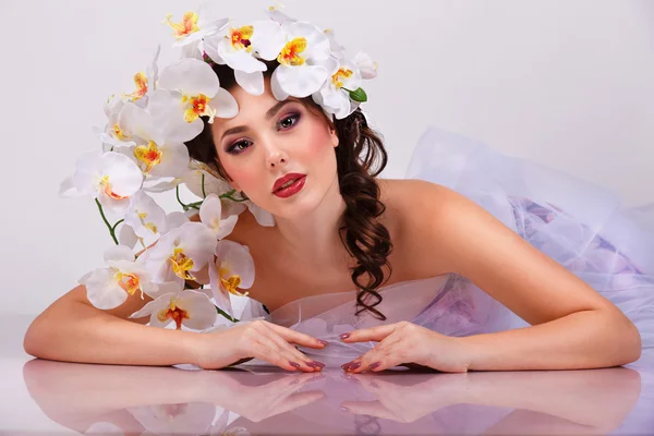 Beautiful sexy brunette woman with orchids flower in her hair and her reflection in mirror table — Stock Photo, Image
